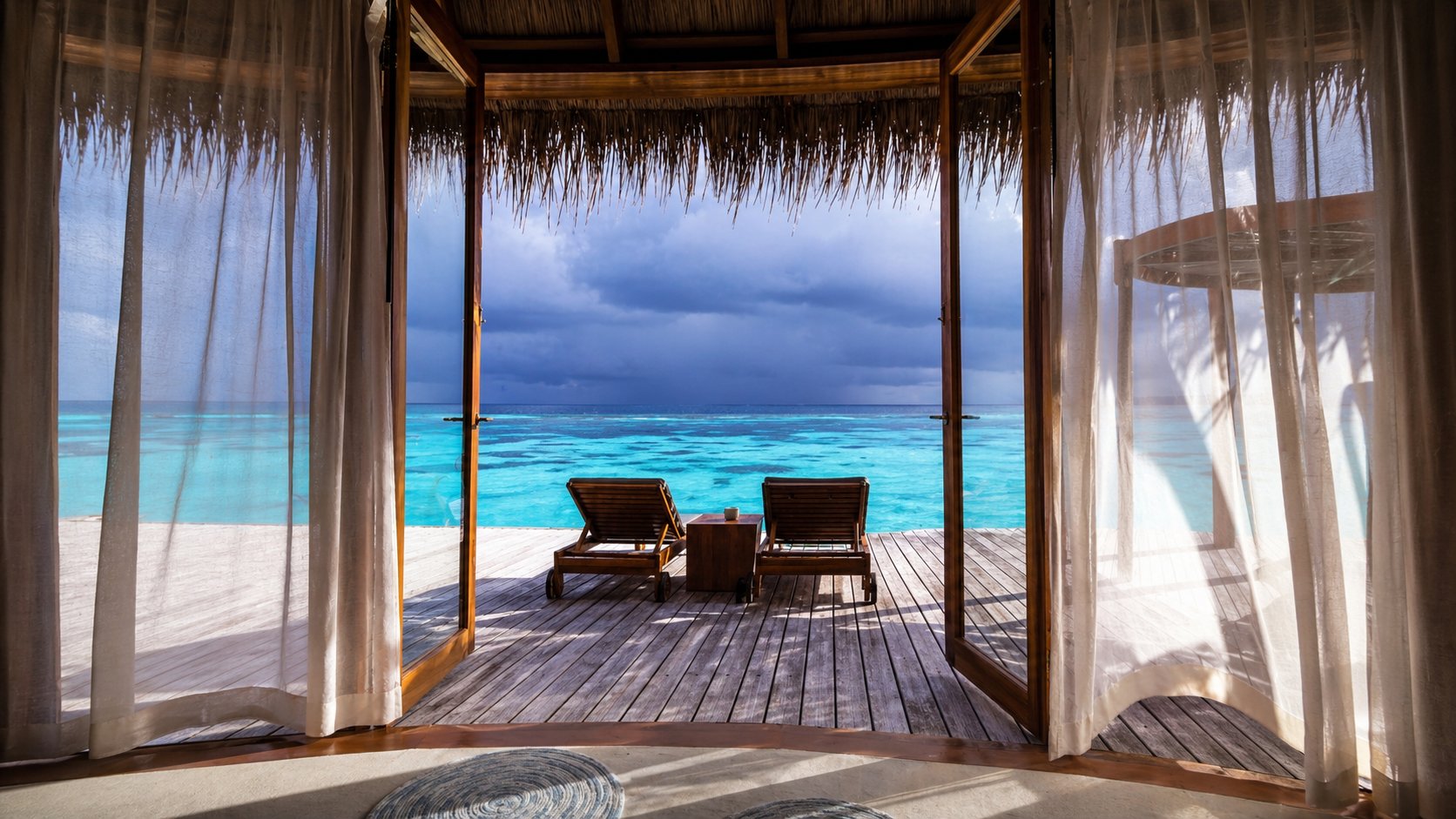 Overwater villa deck with two sun loungers looking out to turquoise ocean